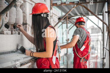 Two workers standing on scaffolding, perform work on the restoration of the facade of the old building. Repairing and renovate Stock Photo