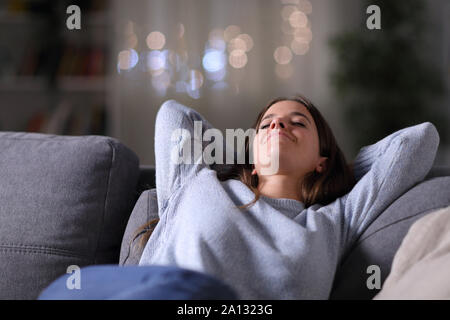 Happy relaxed woman resting sitting on a couch at home in the night