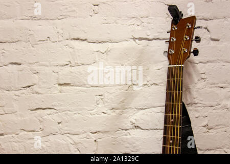 Guitar headstock and neck against white background. Musical instruments stands leaning on brick wall with empty copy space to add text of image. Music Stock Photo