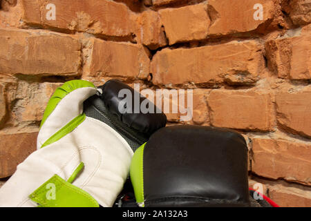 Pair of new boxer gloves against a brick wall. Two multicolored boxing gloves are in a corner of gym hall. Sports equipment closeup image with copy sp Stock Photo