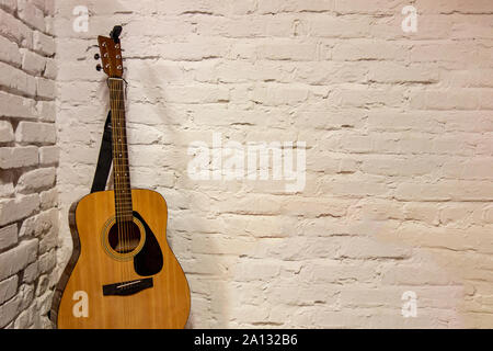 Guitar against white background. Acoustic musical instruments stands leaning on brick wall with empty copy space to add text of image. Music backdrop Stock Photo