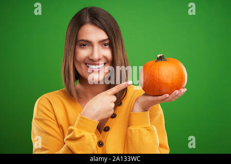 Close up of woman in yellow sweater holding pumpkin over green background Stock Photo