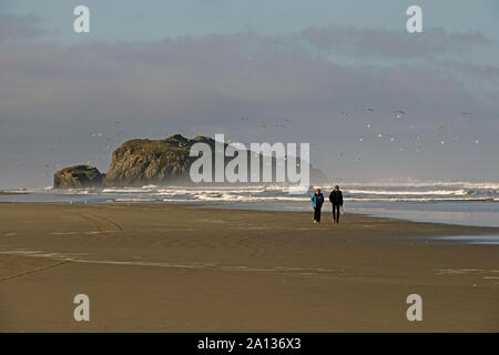 A middle aged couple wander along the empty Pacific Ocean beach in Bandon, Oregon, along the Oregon Pacific Coast. Stock Photo