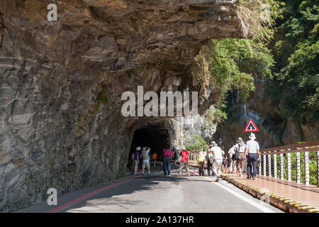 A group of photographers trying to take shot of cliffside tunnel on road under rock overhang along marble canyons, Taroko National Park, Taiwan Stock Photo
