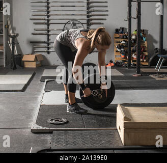 Young strong woman loading weights onto barbell in a gym. Stock Photo