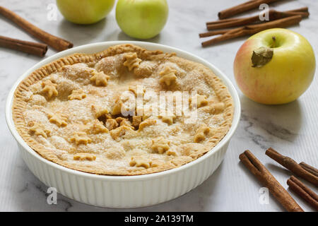 A traditional American apple pie decorated with stars and sugar, apples and cinnamon on a light background. Stock Photo