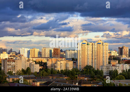 The beautiful light of the setting sun breaks through the heavy autumn clouds and falls on the houses in the city landscape. Stock Photo