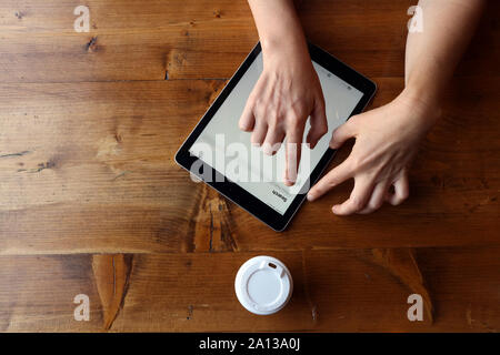 Woman using tablet on rustic wooden background with paper cup of coffee and plastic cup cover Stock Photo
