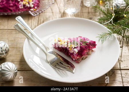 Traditional Soviet festive salad of herring and vegetables, served with vodka in a New Year's decoration. Rustic style. Stock Photo