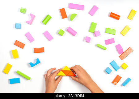 Kid hands playing with colorful wooden building blocks on white table background. Top view Stock Photo
