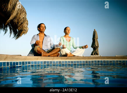 A couple is meditating near the swimming pool on a sunny day. Stock Photo