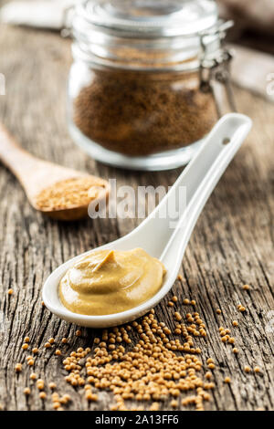 Yellow mustard in ceramic spoon and mustard seeds on old wooden table. Stock Photo