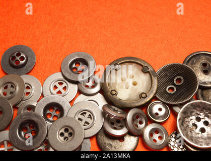 Metal buttons lie on orange felt. An orange background and silver buttons of various shapes. Stock Photo