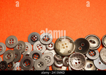 Metal buttons lie on orange felt. An orange background and silver buttons of various shapes. Stock Photo