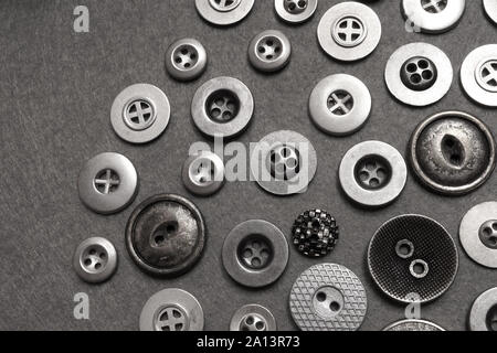 Metal buttons lie on orange felt. Grey background and silver buttons of various shapes. Stock Photo