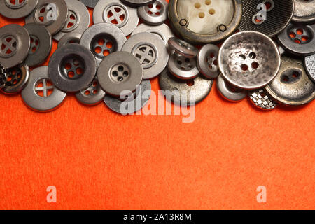 Metal buttons lie on orange felt. An orange background and silver buttons of various shapes. Stock Photo