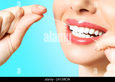 Young beautiful woman is engaged in cleaning teeth. Beautiful smile healthy white teeth. A girl holds a dental floss. The concept of oral hygiene. Stock Photo