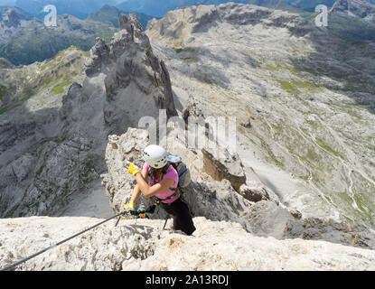 Horizontal view of attractive brunette female climber on a steep and exposed Via Ferrata in the Dolomites pointing to the distance Stock Photo