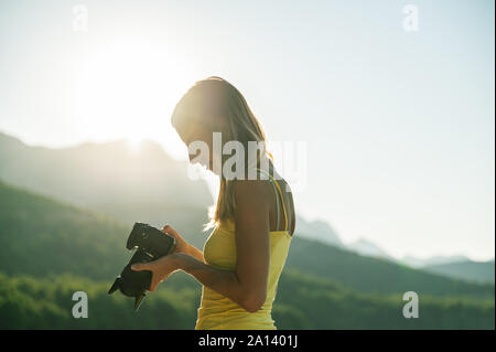 Young female photographer standing outside at sunrise checking a photo on camera display. Stock Photo