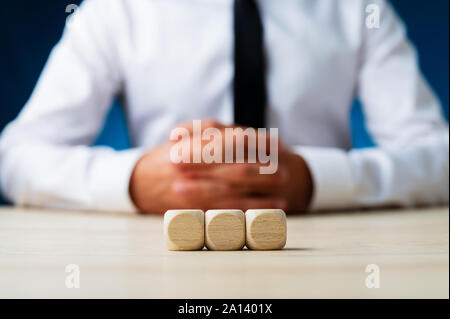 Three blank wooden dices in a row with blurred businessman in background. Stock Photo