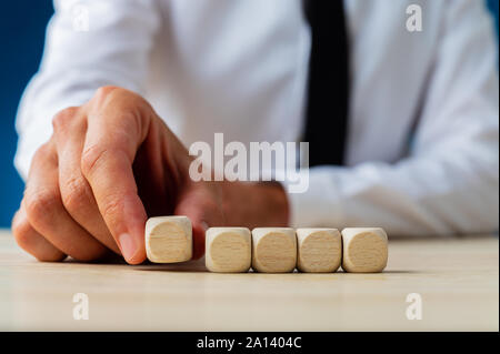 Businessman placing five blank wooden dices in a row on a desk in a conceptual image of business advertisement. Stock Photo
