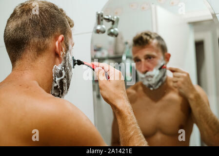 Man shaving face in bathroom mirror Stock Photo