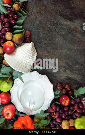 Happy Thanksgiving background with autumn fall leaves, fruit, nuts and tableware on dark slate, vertical copy space. Stock Photo