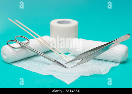 Bandages with forceps and scissors on aqua background. Stock Photo