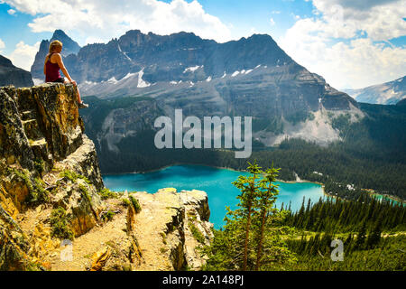 Hiker on a ledge looking at a mountain valley. Lake O’Hara, Yoho National Park, Canada Stock Photo