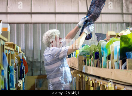A glass artist wears gloves to protect his hands, and examines the colors and patterns in pieces of stained glass, trying to find the perfect piece Stock Photo