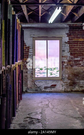 An old brick room with lit window and broken cement floor, houses sheets of stained glass at an old factory in the USA Stock Photo