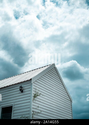 White wooden cabin against the cloud and blue sky background. Rain storm coming with dark clouds above white wooden house. Stock Photo