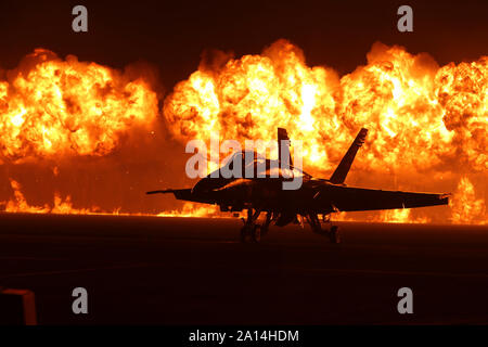 Flames explode behind an F/A-18 Hornet of the U.S. Navy Blue Angels. Stock Photo