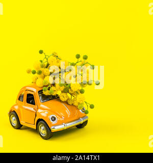 Moscow, Russia - February 23, 2019: 8 March International Women's Day card with toy model of retro car delivering bouquet of mimosa flowers on yellow Stock Photo