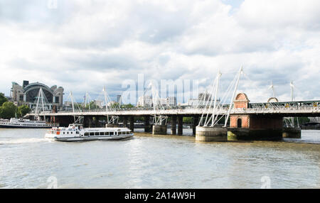 Golden Jubilee Bridges and Charing Cross Station. A touring boat is about to pass under the bridge. Hungerford Footbridges. Stock Photo