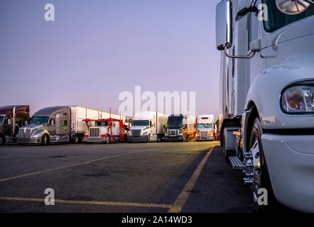 Different make and models big rigs semi trucks with semi trailers standing in row on truck stop parking lot for rest and comply with the movement acco Stock Photo