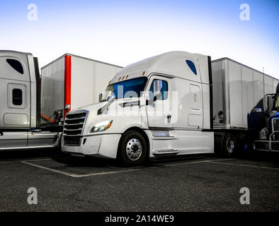 Different make and models big rigs semi trucks with semi trailers standing on the truck stop parking lot under the lighted shelter in night and comply Stock Photo