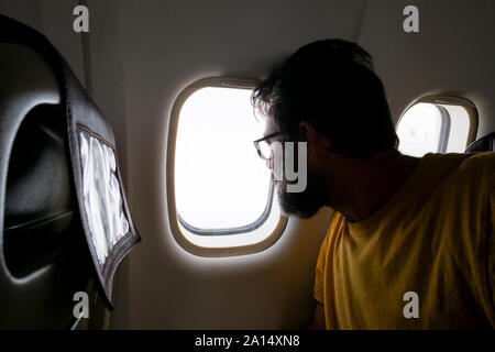 Bearded traveler man look outside the window inside the aiplane flying and traveling - tourism and vacation rtip concept with adult people and flights Stock Photo
