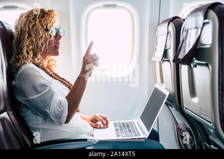 Beautiful female passeger of airplane use personal laptop computer on board with wifi internet connection and ask for hostess help - travel for busine Stock Photo