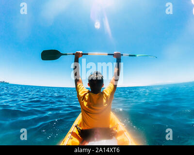 Rear view of tourist man giving up arms enjoying the  kayak excursion in the blue ocean water - concept of happiness for travel and leisure activity o Stock Photo