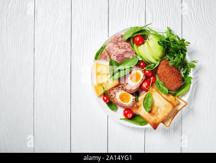 toasts, cheddar cheese, apple, scotch eggs, sliced head cheese, tomatoes, spinach, hot mustard, pickled onion, traditional ploughman's lunch on a plat Stock Photo