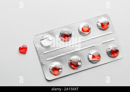 Love pills. Blister pack with red heart shaped pills. Tablets for lovers or potency. Gray background. Stock Photo