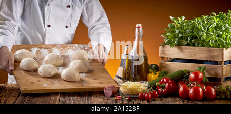 Chef preparing fresh raw dough for pizzas in a pizzeria carrying a board with individual portions to a table with fresh topping ingredients in a panor Stock Photo