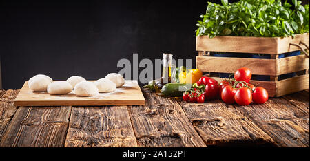 Fresh ingredients for Italian vegetarian pizzas with individual portions of raw dough on a tray, basil, tomatoes, sweet pepper, brinjal, and courgette Stock Photo