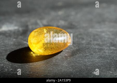 Yellow amber stone with lenticular inclusions, on gray slate background, lit by the sun Stock Photo