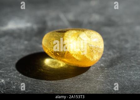 Yellow amber stone with lenticular inclusions, on gray slate background, lit by the sun Stock Photo