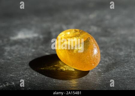 Yellow amber stone with lenticular inclusions, on gray slate background, lit by the sun Stock Photo