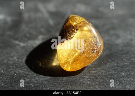 Amber stone with cracked surface, on gray slate background, lit by the sun Stock Photo