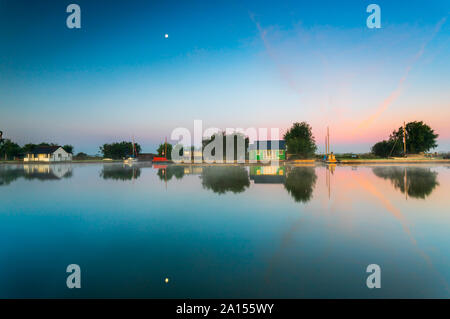 The moon reflection over the River Thurne with boat houses on the shoreline at sunrise on a cold September morning Stock Photo