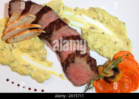 Appetizing steak medium roast, cut into pieces in creamy mushroom sauce. Steak in a white plate on a wooden table. Stock Photo